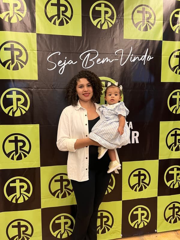 Mãe com bebê no colo diante do painel Seja Bem-Vindo