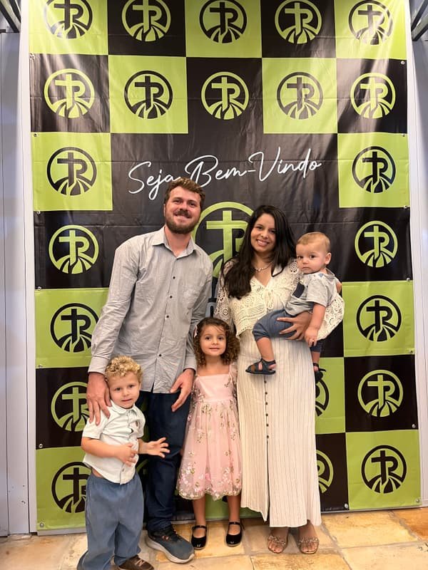 Família com três crianças diante do painel Seja Bem-Vindo